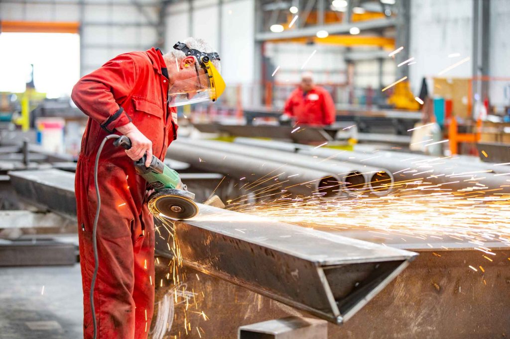 Photograph of steel fabricator grinding excess steel from welding on steel girder