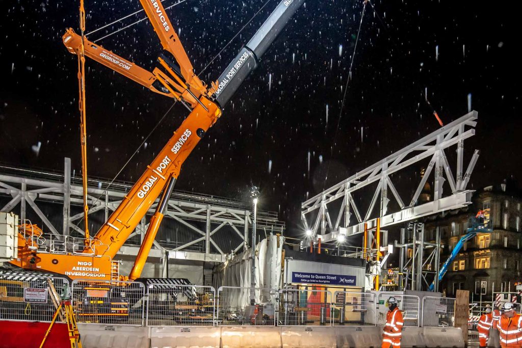 Queen Street Station Glasgow 100-tonne steel truss installation at night in heavy rain showing crane operations and construction workers in extreme weather conditions