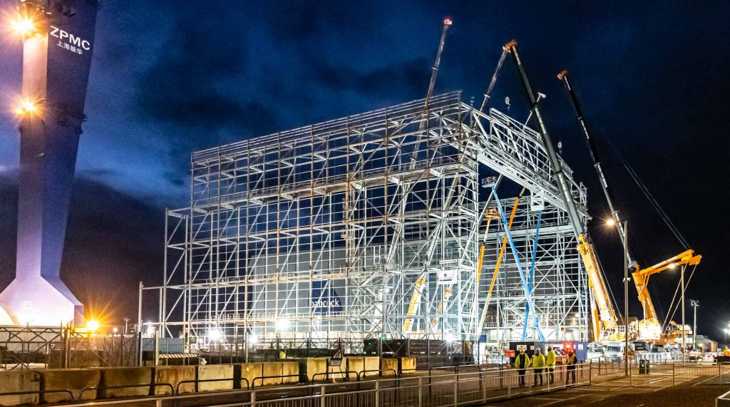 Rosyth Naval Base extension under construction at night showing massive steel framework structure with multiple tower cranes for strategic defense infrastructure