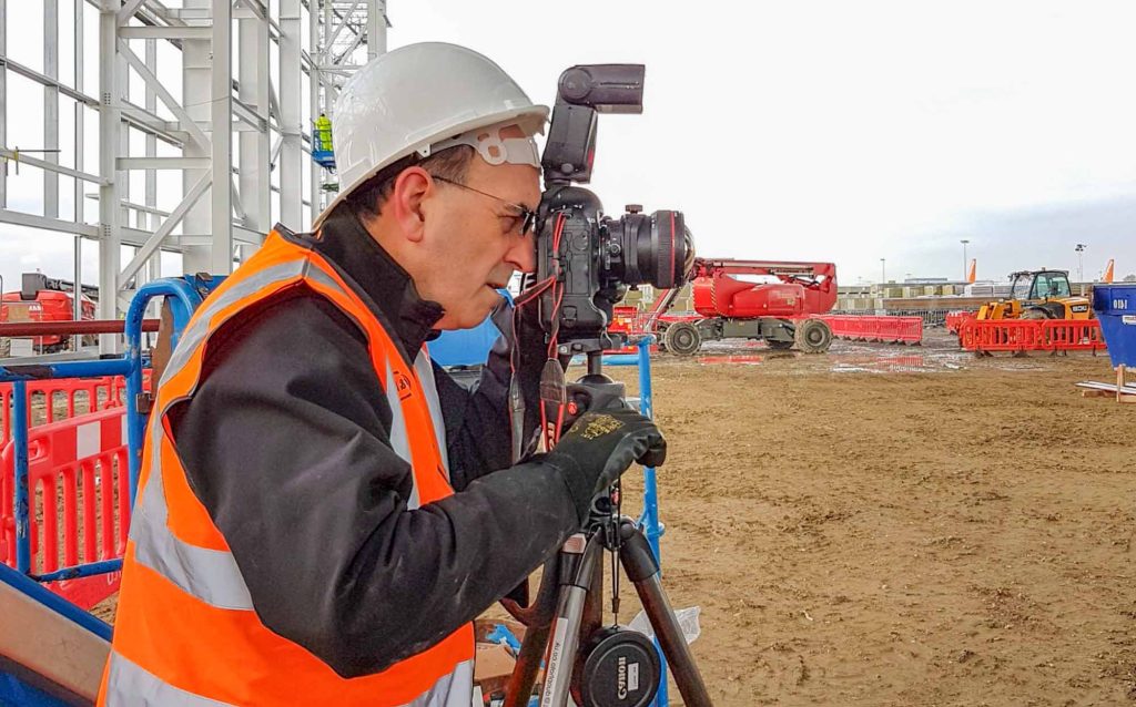 Award-winning construction photographer James Thompson in full PPE documenting major infrastructure construction project, demonstrating professional site safety compliance and technical expertise for London construction photography services