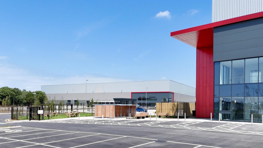 Red entrance cladding in sunlight with the second Arrow Point Bolton logistics unit beyond