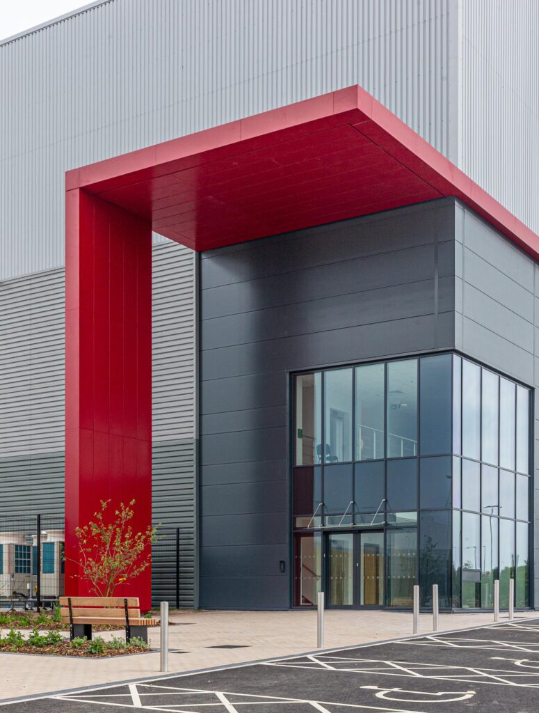 Red-framed main entrance at Arrow Point Bolton showing glazing and completed cladding